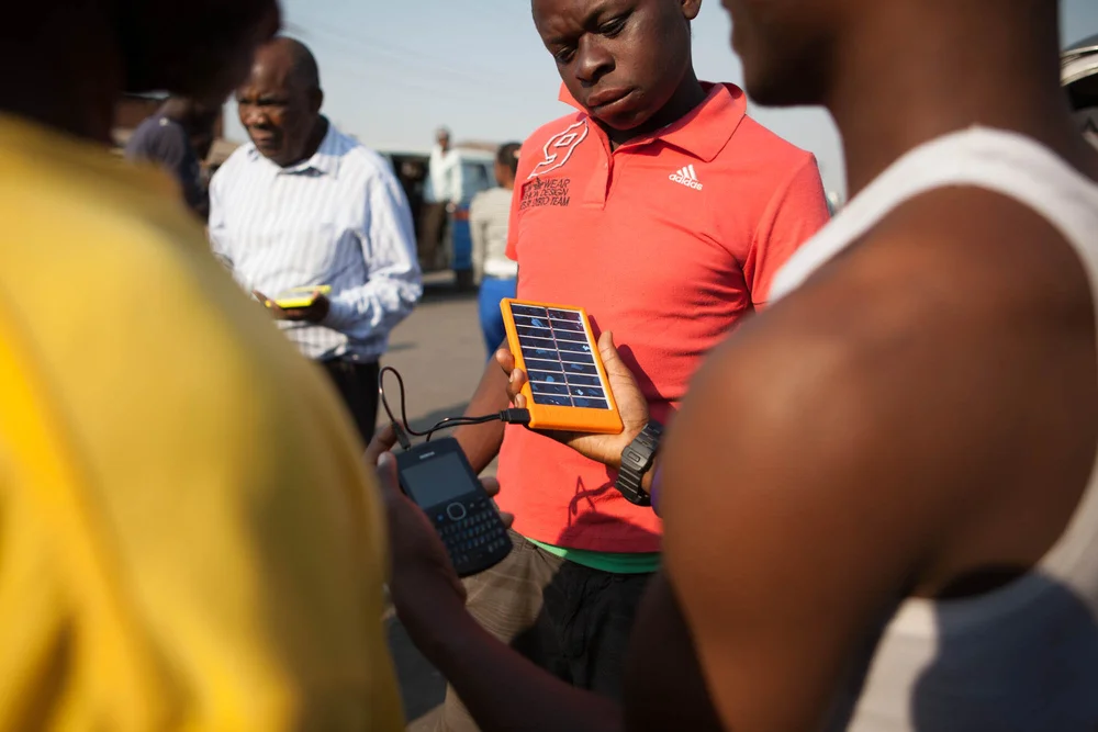 A group on a street examining a solar panel in an orange bumper cabled to a black phone