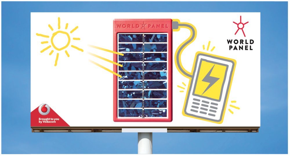 World Panel billboard mock-up against a blue sky: a drawn yellow sun beaming into a red solar panel cabled to a phone, with “Brought to you by Vodacom” in the corner
