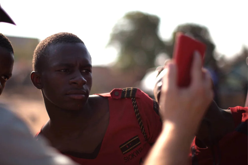 A young man in a red uniform shirt looking at a red phone held up in front of him