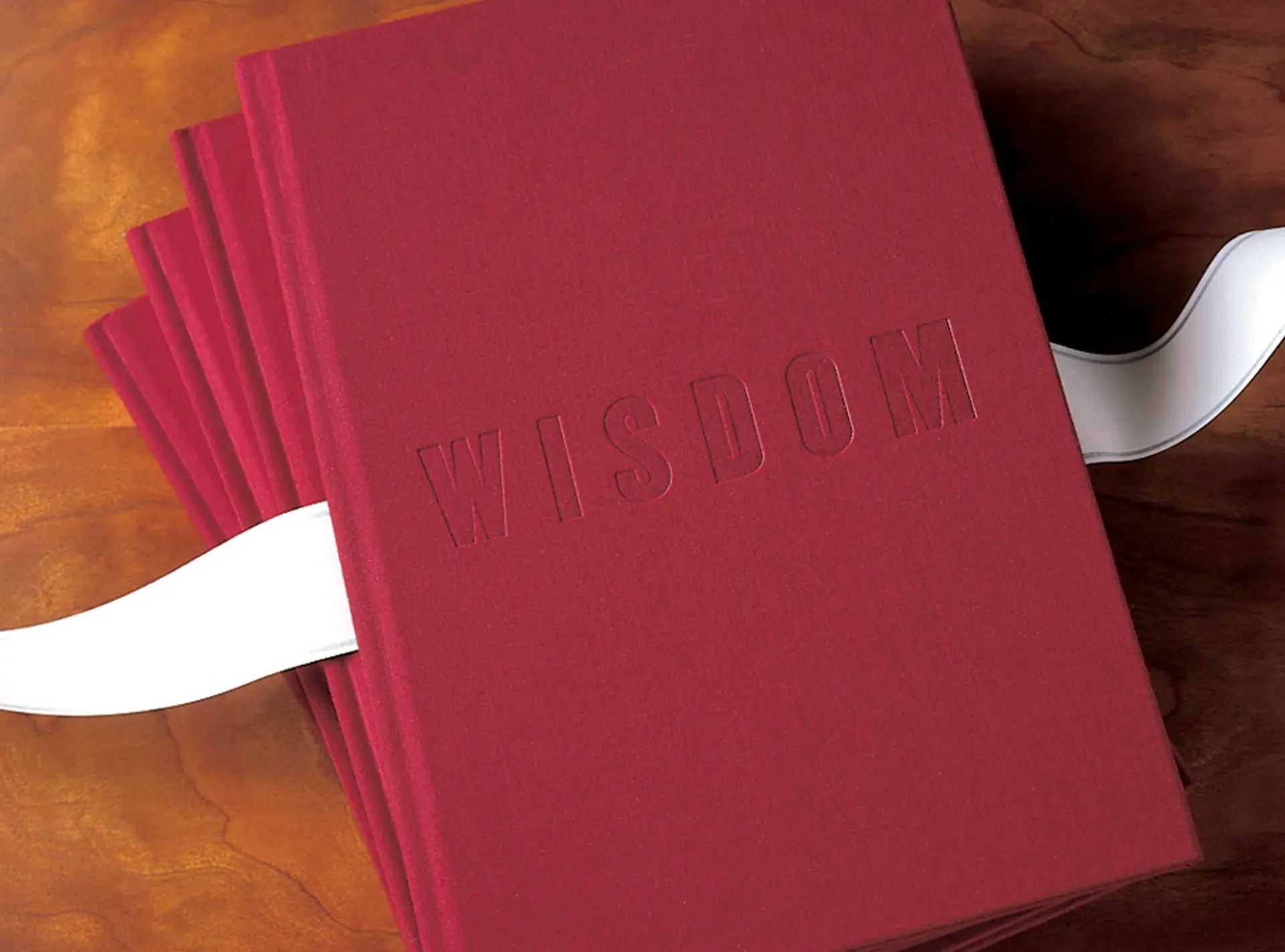 Morton Clarke Advisors: crimson cloth-bound books stacked on a wood table with a white ribbon and “WISDOM” debossed on the cover