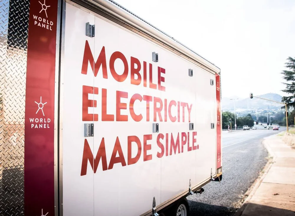World Panel mobile electricity trailer parked at a roadside: “MOBILE ELECTRICITY MADE SIMPLE.” in bold red letters on a white trailer side, with the World Panel name and star mark repeated on a red stripe